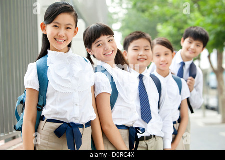 Niedliche Schulkinder in Uniform an einen Zaun gelehnt Stockfoto