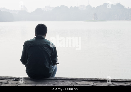 Ein Künstler sitzt am Ufer des Hoan Kiem See im Zentrum von Hanoi zu skizzieren Sie den See und die Turtle Tower in den Morgennebel... Der See ist bekanntlich in der vietnamesischen Ho Hoan Kiem See des zurückgegebenen Schwertes bedeutet. Stockfoto