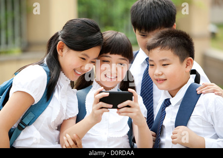 Aufgeregt Schulkinder in Uniform mit Smartphone auf Schulhof Stockfoto