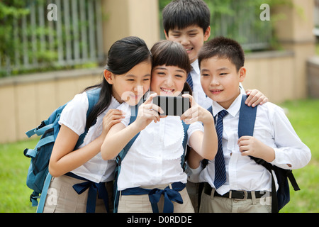 Aufgeregt Schulkinder in Uniform macht eine Selbstporträt Fotografie mit Smartphone Stockfoto