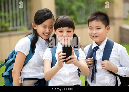 Aufgeregt Schulkinder in Uniform mit Smartphone auf Schulhof Stockfoto