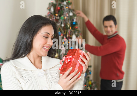 Frau hält ein Geschenk während ihr Ehemann dekorieren Weihnachtsbaum Stockfoto