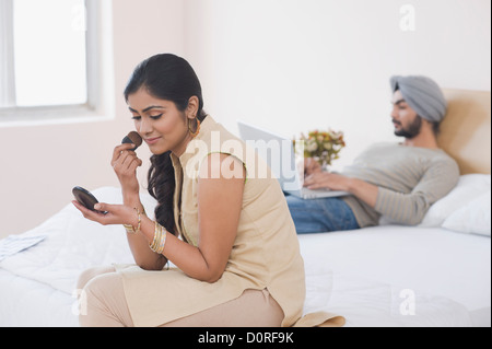 Frau Schminken während ihr Mann arbeitet an einem Laptop auf dem Bett Stockfoto