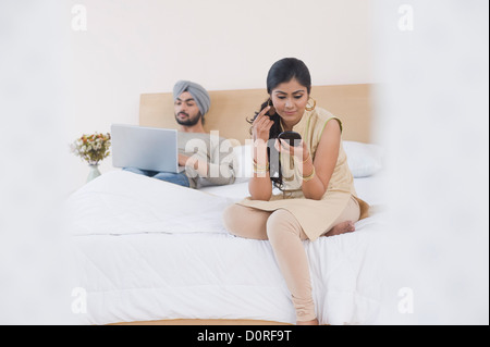 Frau Schminken während ihr Mann arbeitet an einem Laptop auf dem Bett Stockfoto