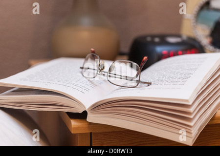 Nachtzeit lesen, lesen im Bett. Taschenbuch mit Lesebrille auf Nachttischen. Stockfoto