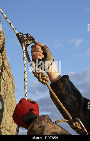 Hände des Kletterers arbeite ich mit Ausrüstung auf Felsen. Stockfoto