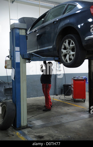 Kfz-Mechaniker, die Reparatur eines Autos auf einer Hebebühne angehoben Stockfoto