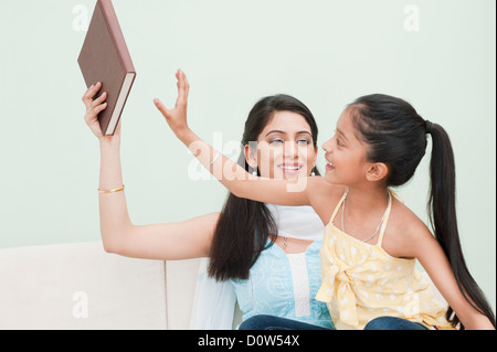 Mädchen für ein Buch in der Hand der Mutter zu erreichen Stockfoto