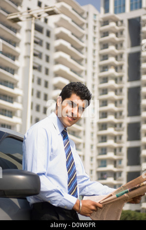 Geschäftsmann, lesen eine Zeitung neben einem Auto, Gurgaon, Haryana, Indien Stockfoto