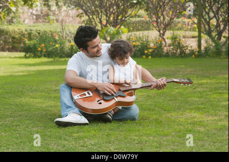 Mann, eine Gitarre zu spielen, mit seinem Sohn auf dem Schoß sitzen Stockfoto