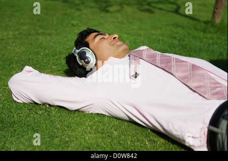 Geschäftsmann hören über Kopfhörer in einem Park, Gurgaon, Haryana, Indien Stockfoto