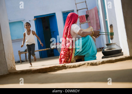 Frau Butter Buttern, mit ihrem Sohn spielen hinter ihr, Farrukh Nagar, Gurgaon, Haryana, Indien Stockfoto