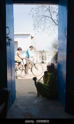 Frau raucht eine Pfeife Wasserpfeife mit Kinder Fahrrad fahren, Farrukh Nagar, Gurgaon, Haryana, Indien Stockfoto