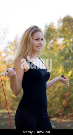 Formschöne blonde Frau im Sport Getriebe stehen mit einem Springseil in den Händen in einem park Stockfoto