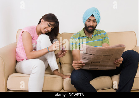 Sikh Mann liest eine Zeitung und eine Frau malt ihre Fingernägel Stockfoto