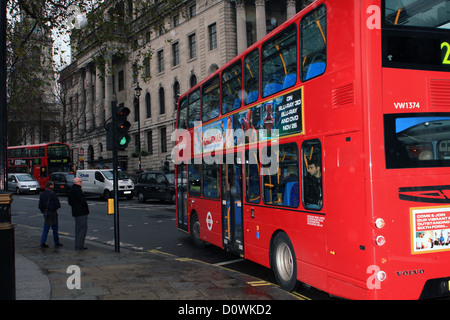 Einem roten Londoner Doppeldeckerbus grüne Ampeln vorbei, während zwei Personen warten auf die Straße zu überqueren. Stockfoto