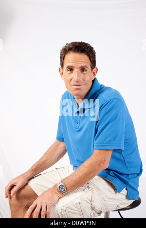 Gut aussehender Mann in blauen Golf-Shirt, mit seinen Händen auf den Knien und schaut in die Kamera mit einem zufrieden Ausdruck Stockfoto