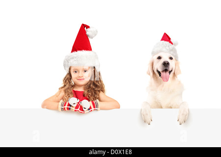 Mädchen und Hund Santa Hüte tragen und posiert hinter eine Blindplatte Stockfoto