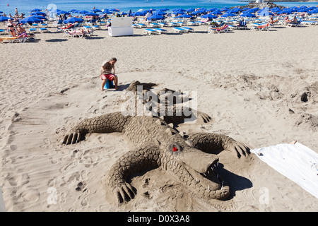 Künstler machen eine Sandskulptur von einem riesigen Krokodil oder Alligator am Strand von Playa Las Vistas in Los Cristianos, Teneriffa, Stockfoto