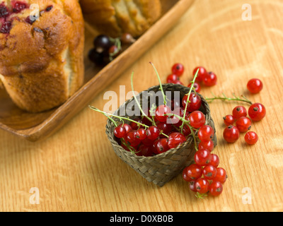 Detail aus einem Haufen von Johannisbeeren in einem Korb auf einem Holztisch mit Muffins auf einem Teller hinter den Korb Stockfoto