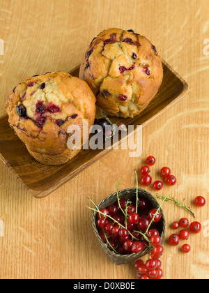 obere Ansicht von paar Muffins auf einem Teller, in der Nähe einen Korb, gefüllt mit roten Johannisbeeren, auf einem Holztisch Stockfoto