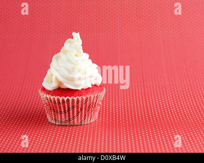 Nahaufnahme von einen einzigen winzigen Velvet Cupcake mit Sahnehäubchen obendrauf, weiß auf rot Tupfen Hintergrund isoliert Stockfoto