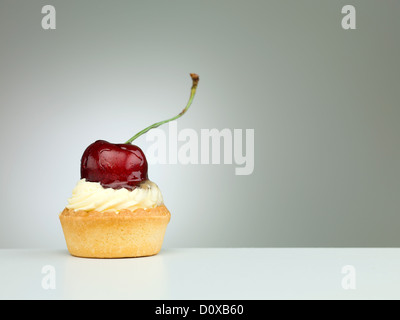 Nahaufnahme einer winzigen Torte mit Sahnehäubchen, platziert auf einem weißen Tisch mit Farbverlauf Licht auf neutralem Hintergrund Stockfoto
