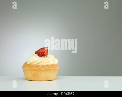 Nahaufnahme einer winzigen Torte mit Erdbeeren obendrauf, platziert auf einem weißen Tisch mit Farbverlauf Licht auf neutralem Hintergrund Stockfoto