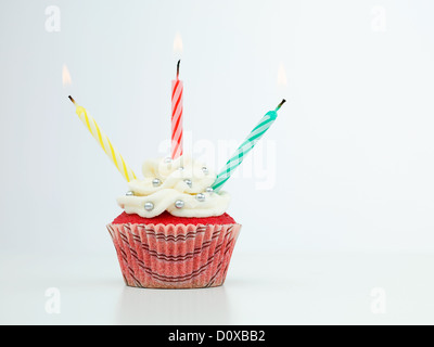 roten Muffin mit drei Kerzen, die isoliert auf weißem Hintergrund Stockfoto