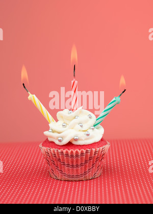 Muffin auf roten Tisch mit drei Kerzen auf rosa Hintergrund Stockfoto