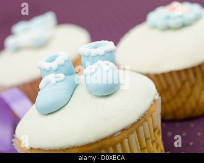 drei Muffins für Neugeborene Urlaub im Vordergrund blau Hausschuhe lila Hintergrund Stockfoto