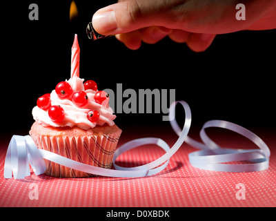 Hand mit einem Feuerzeug, Kerze Blueberry Muffins blaues Band rot weiß gepunkteten roten Tisch und schwarzem Hintergrund zu beleuchten Stockfoto