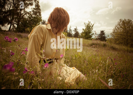 Junge Frau sitzt im Feld, wegschauen Stockfoto