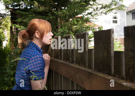 Junge Frau, die über den Zaun in Nachbars Garten Stockfoto