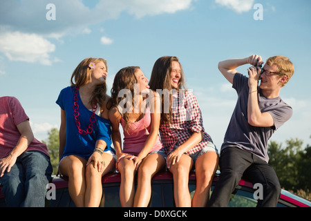 Freunde sitzen auf Autodach, jungen Mann Fotografieren Stockfoto