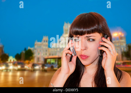 Junge Frau mit zwei Handys am Cibeles-Platz. Madrid, Spanien. Stockfoto