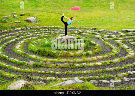 Frau mit Regenschirm in Yoga-Pose im Zentrum von Stein Labyrinth Stockfoto