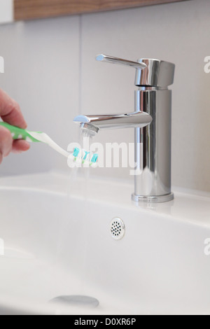 Fließendes Wasser auf Zahnbürste in Waschbecken Stockfoto