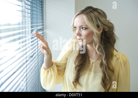 Büroangestellte sucht durch die Jalousien von ihrem Bürofenster. Stockfoto