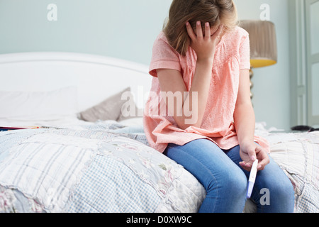 Teenager-Mädchen sitzen auf dem Bett mit Schwangerschaftstest Stockfoto