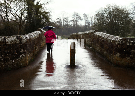 Frau im roten Mantel zu Fuß über eine Brücke in Regen Stockfoto