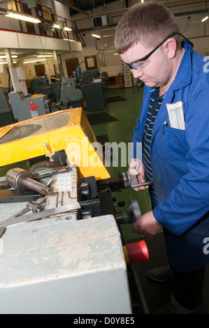 Junger weißer Mann im blauen Overall in einer Fabrikhalle auf einem Engineering Ausbildung Tragen von Schutzbrillen, die der Betrieb einer Maschine Stockfoto