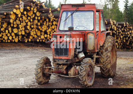 alte beschädigte Traktor auf einer Bergstraße und einen Stapel gefällter Bäume im Hintergrund Stockfoto