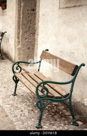 Hölzerne Sitzbank sitzt auf alten Kopfsteinpflaster gegen dicken Steinmauer im zentralen Innenhof auf der Festung Hohensalzburg. Stockfoto