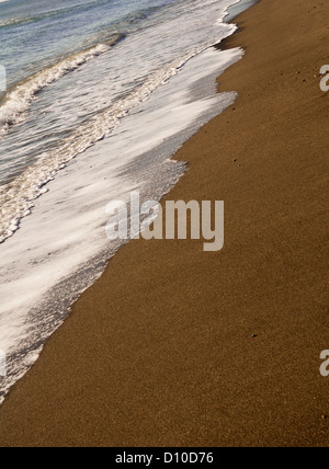 Weiße Wellen brechen sich am Sandstrand Stockfoto