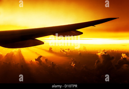 Foto des Flugzeugs in den Abendhimmel, Silhouette der Flugzeugflügel auf Sonnenuntergang, leuchtend gelben Sonnenstrahlen, Unternehmensverkehr Stockfoto