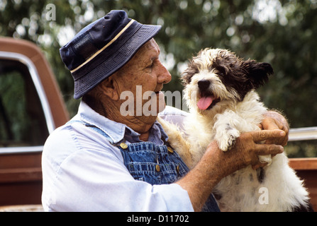 1990ER JAHRE ÄLTEREN MANN TRÄGT HUT UND OVERALLS MIT HUND Stockfoto