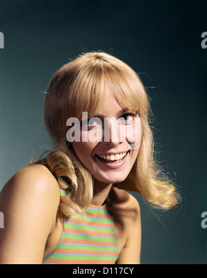 1960ER JAHRE PORTRAIT DER JUNGEN BLONDEN FRAU LÄCHELND TRAGEN GESTREIFTEN ÄRMELLOSES TOP Stockfoto