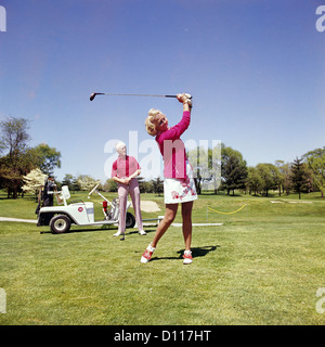 1960S 1970S STEHT REIFE FRAU SCHWINGEN GOLFCLUB AS MANN VON GOLF-CART Stockfoto