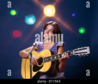 1970ER JAHREN FRAU MÄDCHEN DARSTELLER SPIELEN GITARRE GESANG MIKROFON BÜHNENBELEUCHTUNG Stockfoto